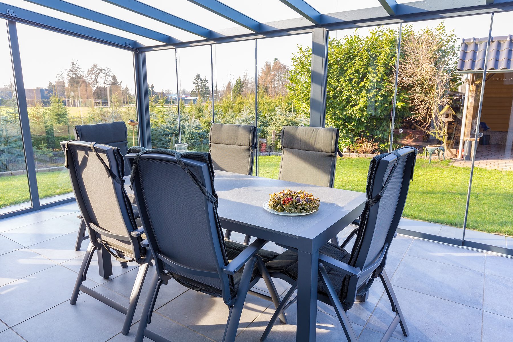 Blick aus dem Inneren eines verglasten Anbaus mit Aluminiumprofilen auf den Garten